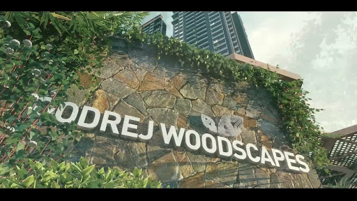 A grand, architectural entrance of Godrej Woodscapes featuring high-quality stone masonry, integrated greenery with ivy and lush plants, and a sophisticated minimalist sign.